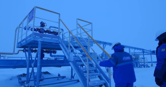 Workers in the gas and oil industries go to the control area on the pipelines of the oil and gas complex. Cold winter outside, snow everywhere