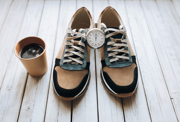 A pair of suede sneakers on a rustic wooden background and a paper cup of coffee and stopwatch The concept of energy drink, sports shoes and thirst.