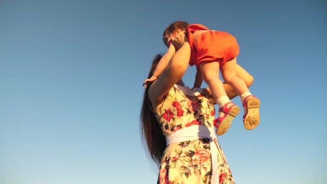 mother plays with a small child against a blue sky. Mom throws her daughter up to the sky. happy family playing in the evening against sky. mother throws up baby, baby smiles. slow motion filming.