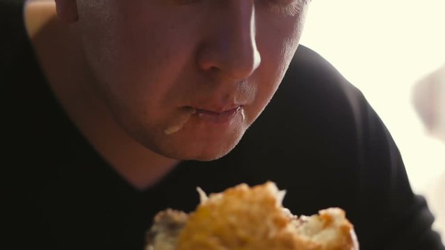 Close-up of the man's face, biting off a delicious juicy Burger.
