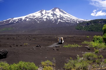 View over wide field of volcanic lava ash with isolated 4 wheel camper on peak of black Volcano...