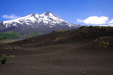 View over wide field of volcanic lava ash hills on peak of black Volcano Llaima with spots and stripes of snow and ice contrasting with blue sky - Conguillio NP in central Chile