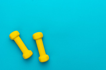 flat lay photo of yellow fitness dumbells over blue backgound with copy space