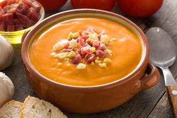 Typical Spanish salmorejo cream with ham and egg on wooden table. 