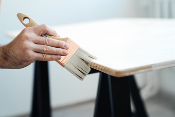 Work painter. Close-up male hand with brush stains wood surface with lacquer or light paint.