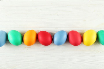 Bunch of blank painted Easter eggs of different pastel color on white wood textured table background with a lot of copy space for text. Top view, flat lay, close up.