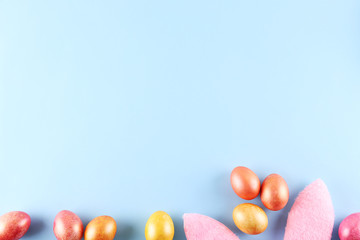 Fluffy Easter bunny ears as symbol of Christian religious holiday. Traditional eggs painted in pink and rose gold colors. Copy space, close up, flat lay, top view, bright colorful background.