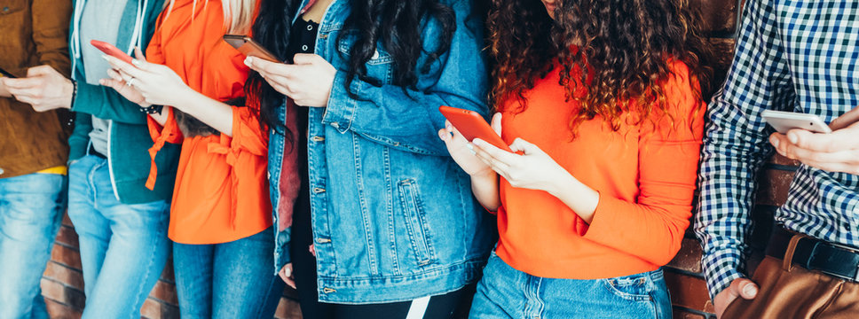 Millennials style. Young people in trendy denim outfits standing with smartphones, reading messages, posts in social networks.