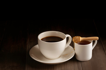 Coffee cup and sweet honey on black wooden background.