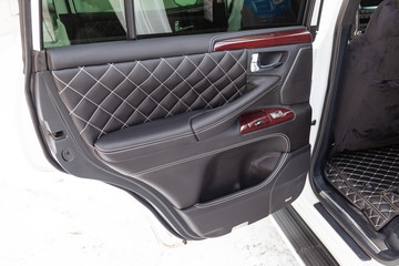 Interior of a luxury car with leather interior overtightened stitching in the form of a diamond of white thread at door trim in a vehicle repair shop. Design atelier auto service.