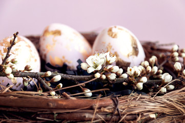 Obraz na płótnie Canvas Gold foiled painted easter eggs in a nest, decorated with a cherry blossom branch.