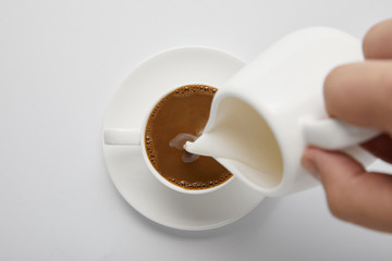 Cropped view of woman pouring milk in coffee on white