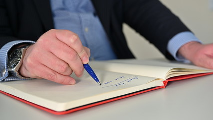 Mann schreibt mit blauem Stift in ein Notizbuch