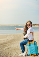 Cute little girl with suitecase on the beach. Summertime concept.