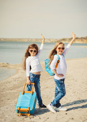 Fototapeta na wymiar Cute little girls with suitecases on the beach are ready to travel. Summertime 