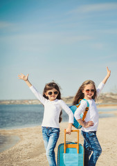 Cute little girls with suitecases on the beach are ready to travel. Summertime 