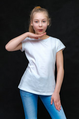 Concept portrait of a cute pretty blonde teen girl with long hair posing in white t-shirt on black background in studio.