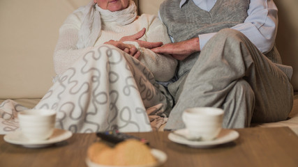 Headless elderly person enjoying time on couch with tea