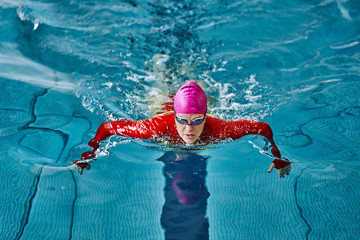 Female athlete in a red-yellow swimsuit is swimming in the style of breaststroke. Splashes of water...