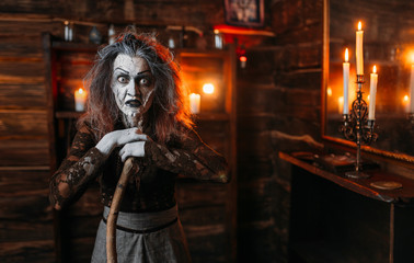 Scary witch with a cane at the mirror and candles
