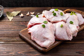 Raw chicken thighs on dark wooden background.