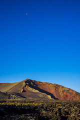 Spain, Lanzarote, Impressive colorful red volcanic crater and moon in early sunrise light