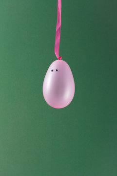 Pink balloon with eyes dangling on green background