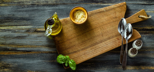 banner of Cutting wooden board from olive wood on a blue wooden table with olive oil, basil and Parmesan cheese. Mediterranean table settingn board from olive wood on a blue wooden table 
