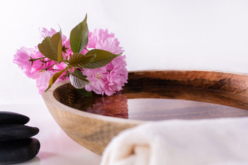 Wooden bowl with water and pink flower and black rock and towel isolated on white background. Natural organic cosmetic, wellness and spa concept. Close up, selective focus