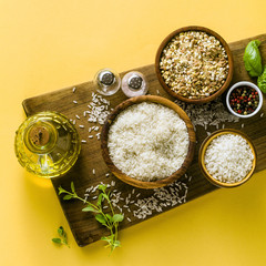 Different types of rice on a wooden board made from olive wood. Food background with basil leaves and olive oil. healthy home cooking