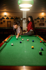 Couple plays in billiard room, male player aiming