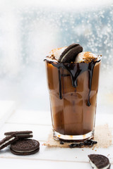 Coffee with marshmallows and pouring chocolate sauce on white wooden tray in front of window on a rainy day.