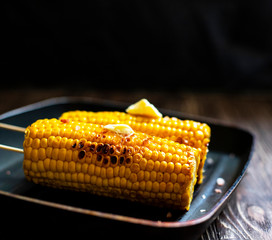 Delicious grilled corn with butter and salt on a grill pan on a rustic wooden background. Closeup