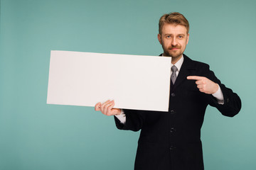 Happy smiling young business man points finger blank signboard