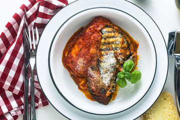 Italian melanzane alla parmigiana dish, made of eggplants and tomatoes on a table, served in a plate. with cheese and basil. traditional cuisine