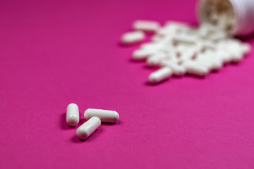 White pills spilling out of a toppled white bottle 