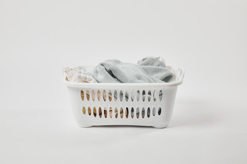 White plastic laundry basket with dirty clothes on grey