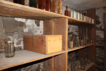 An old shelf in a basement, with empty glass bottles and cans.