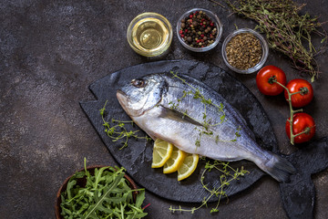 Dorado fish with fresh vegetables and herbs on a dark background