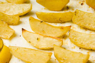 Delicious baked potatoes with rosemary on parchment, closeup. Vegetarian food. Potato country style