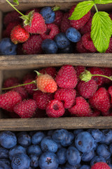 Mix of fresh berries with leaves in vintage wooden box on rustic wooden background. Top view. Raw healthy food. Assorted berries.