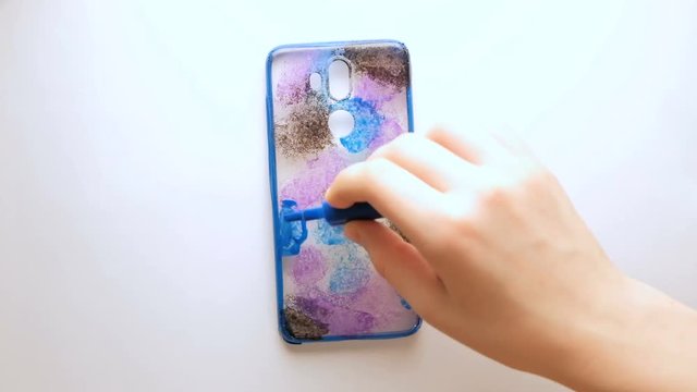 DIY. Coloring the cover for a mobile phone with multi-colored spots. The hands of a teenager. Self-made creativity. Close-up.