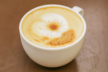 close up of big cup of freshly brewed cappuccino with soft foam and brown sugar on wooden table.