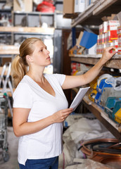 Woman customer  holding  shop list and looking tools at shelves in store