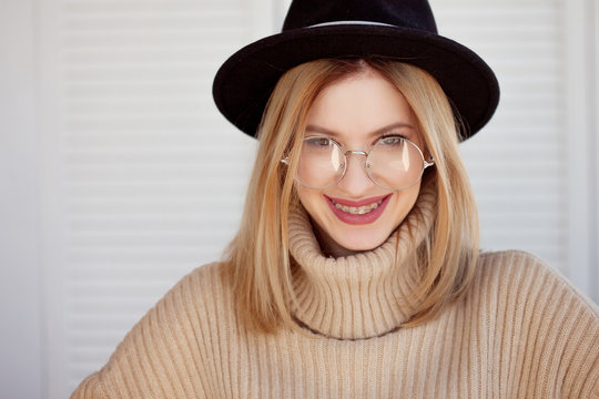 Young cute blonde with eyeglasses and a beige sweater. Stylish fashionable young woman.