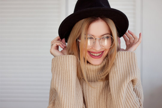 Charming young girl in a stylish hat and glasses. Young woman wearing braces and smiling