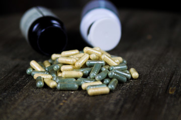 Pile of yellow and green capsules dispersed on wood table with tipped over pill boxes 