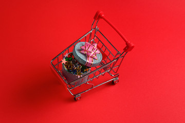 Blue present box with pink bow in a shopping cart on a red background.