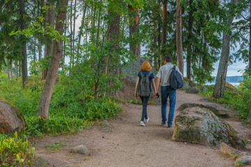 Fototapeta premium Dark-haired middle-aged man and red-haired young lady walk along forest road. Tourists on the beautiful landscape background. Monrepos Park, Vyborg, Russia. Travel concept