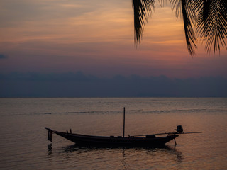 Silhouette of a boat and palm trees against the setting sun with clouds. Koh Phangan. Thailand